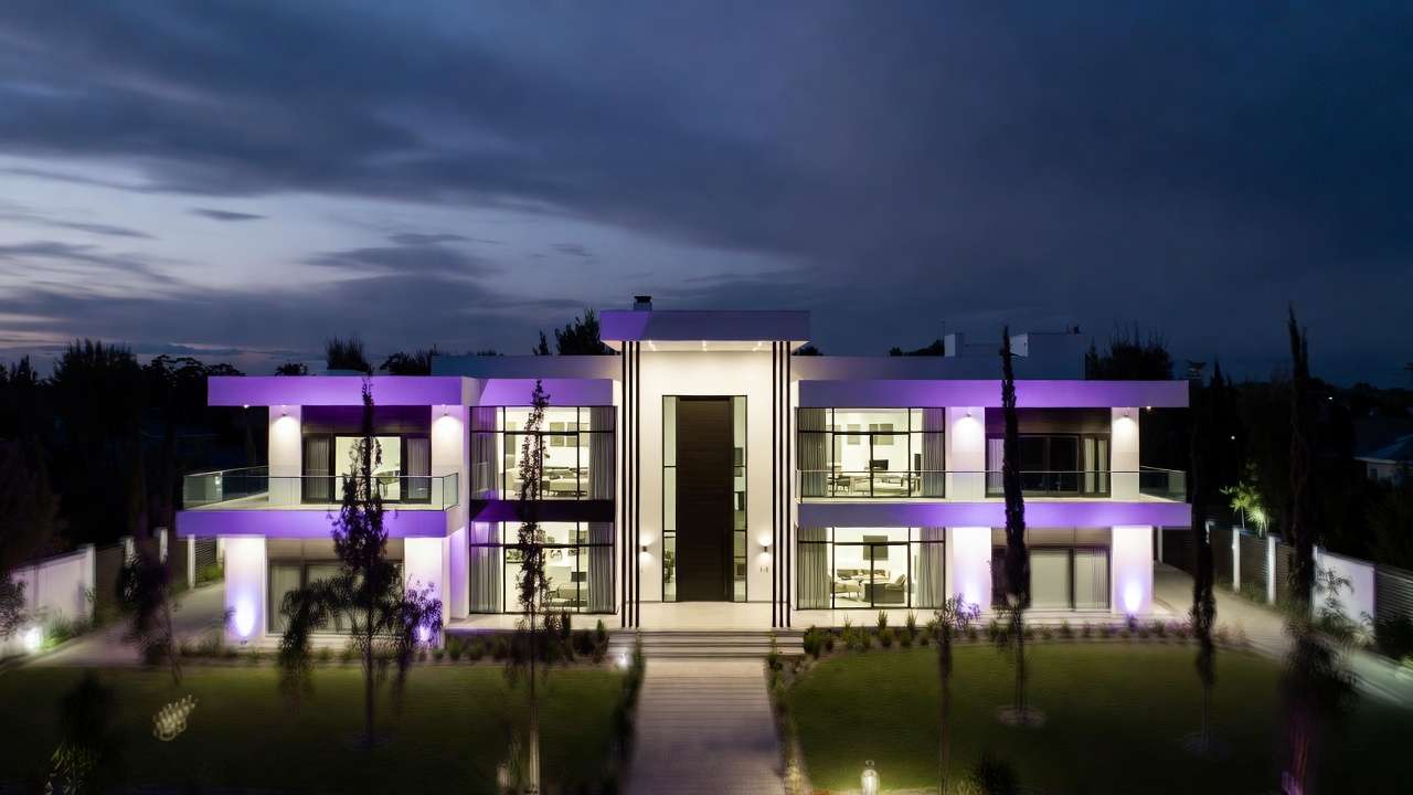 Modern luxury house at twilight with purple LED strip lighting, white facade, dark-framed windows, green lawn