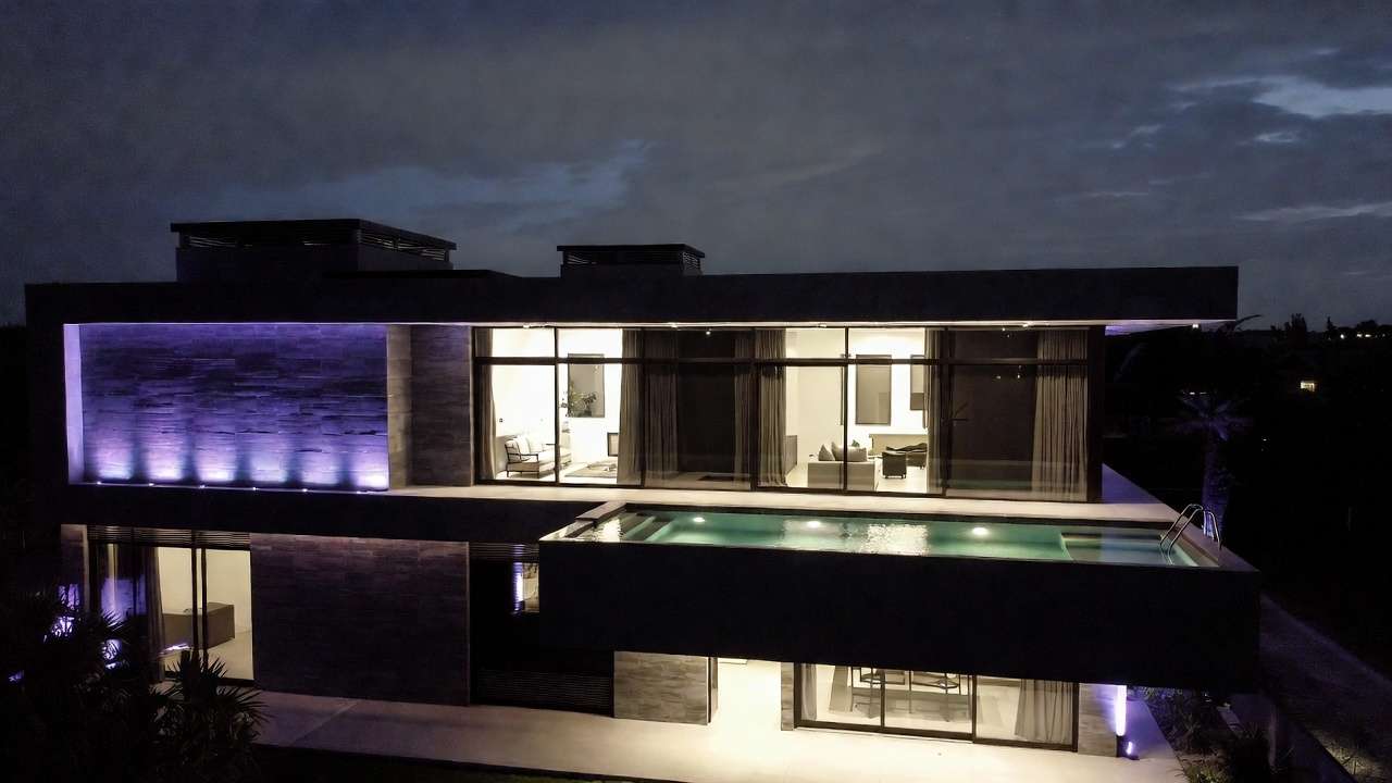 Modern luxury home at night, infinity pool, purple accent lighting on stone facade