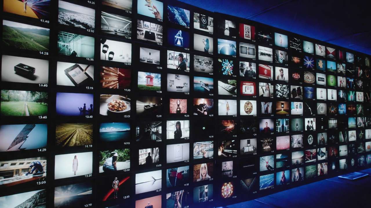 Vast video wall with hundreds of screens showing landscapes, portraits, abstract art, timestamps